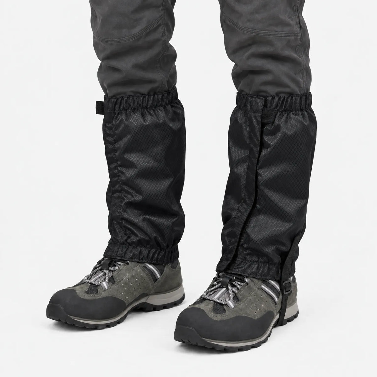Front view of black ripstop gaiters with a strap fastening, worn over grey hiking boots and dark trousers on white. 9