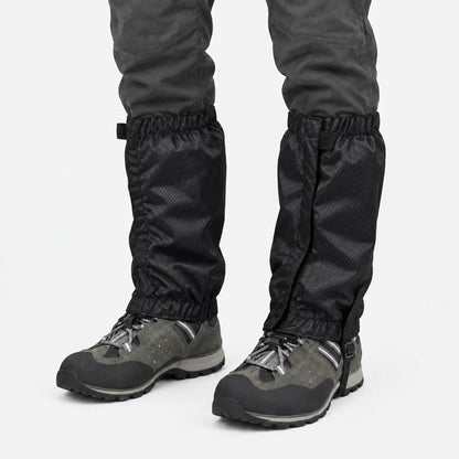 Front view of black ripstop gaiters with a strap fastening, worn over grey hiking boots and dark trousers on white. 9