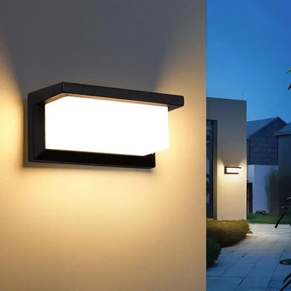 Lit wall light on a cream wall, with a paved garden path and house behind 3