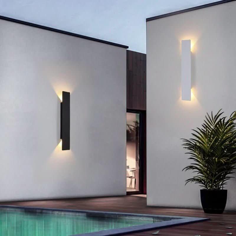 One black and one white wall light on white walls beside a swimming pool, each lit warmly top and bottom. 4