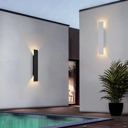 One black and one white wall light on white walls beside a swimming pool, each lit warmly top and bottom. 4