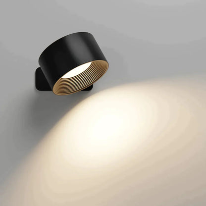Black version of the wall light with a ribbed inner ring, lit and throwing a soft glow down the wall. 2