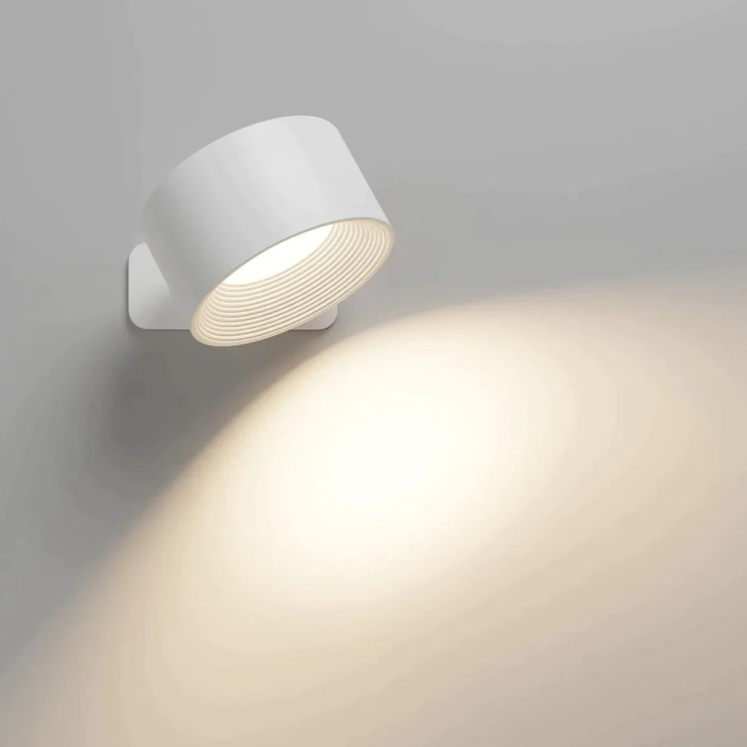 White cylindrical wall light switched on, casting a warm pool of light down the pale wall. 1