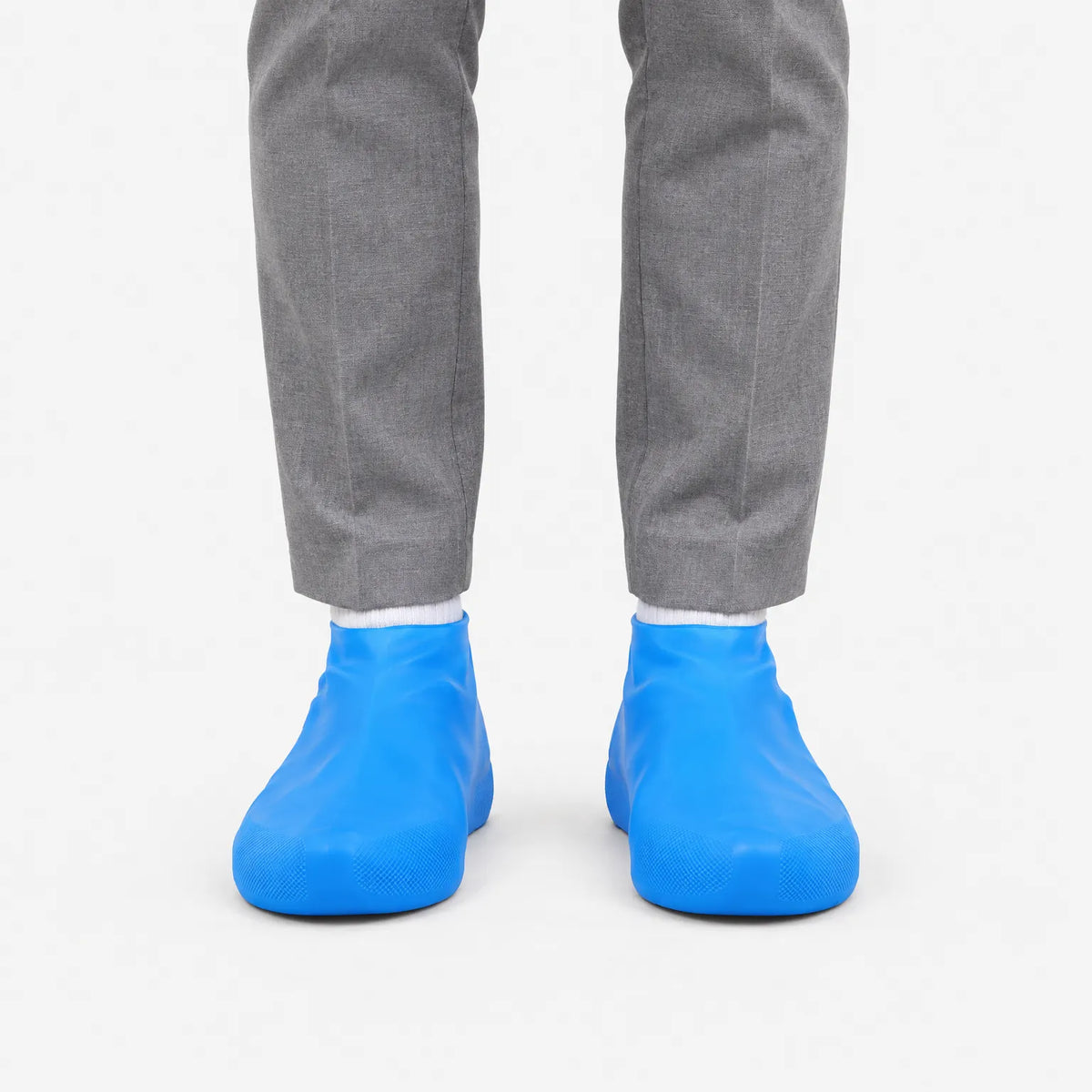 Front view of blue shoe covers worn over shoes with white socks and grey trousers, against a plain white background. 2