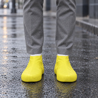 Yellow shoe covers worn on a wet city street, with water droplets beading on the surface and grey trousers above. 3