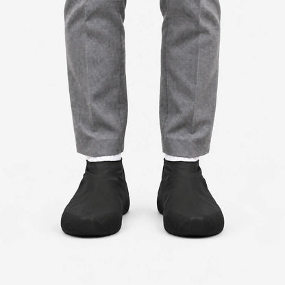Front view of black shoe covers worn with white socks and grey trousers, against a plain white background. 4