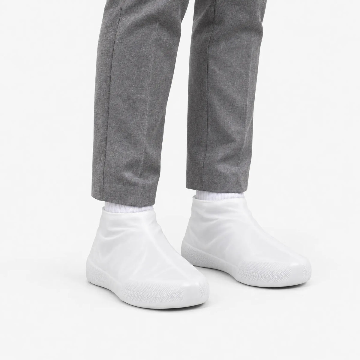Translucent white shoe covers worn at a three-quarter angle with grey trousers, showing the textured grip around the toe. 5