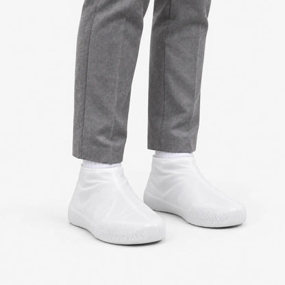 Translucent white shoe covers worn at a three-quarter angle with grey trousers, showing the textured grip around the toe. 5