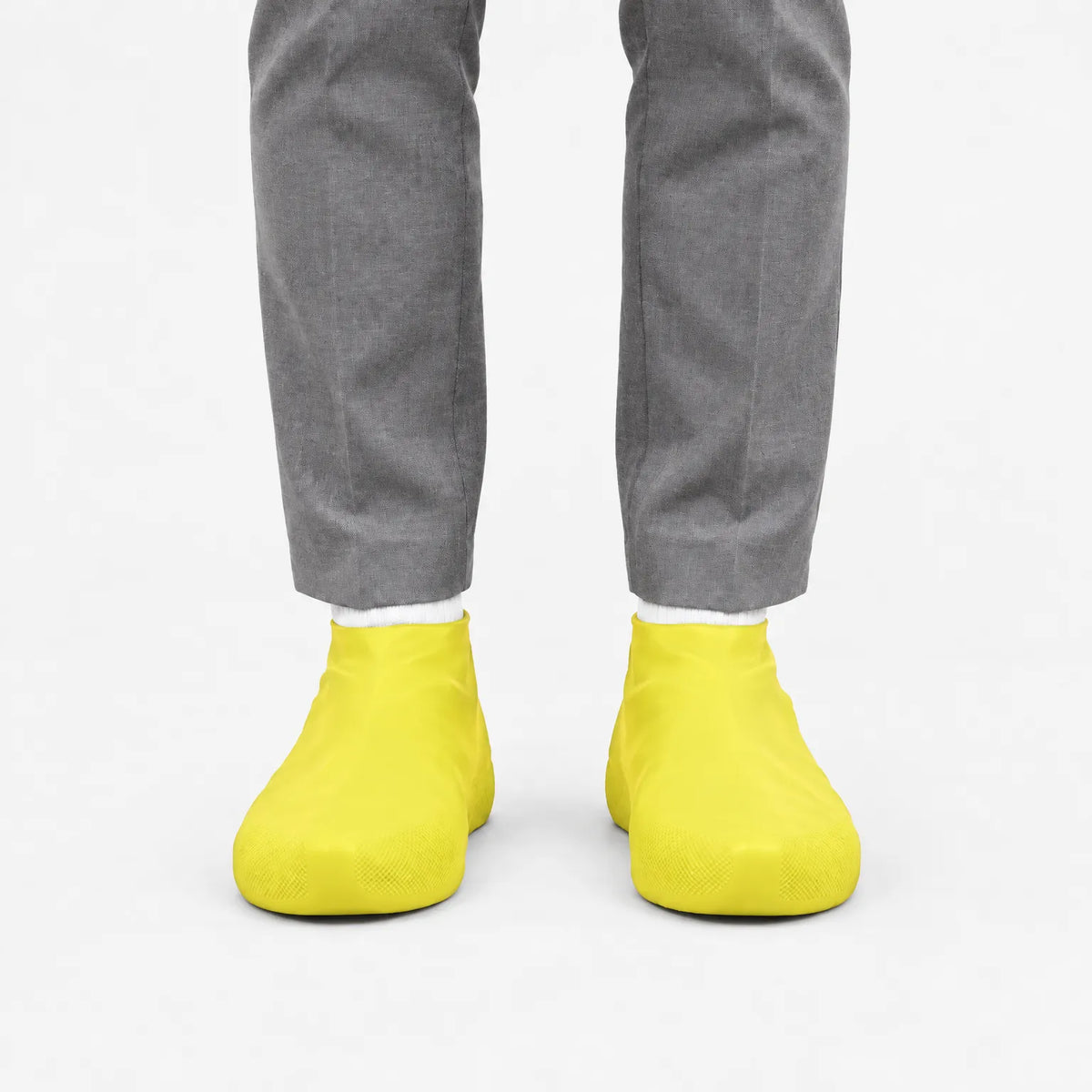 Front view of yellow shoe covers worn with white socks and grey trousers, against a plain white background. 7