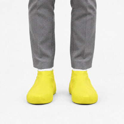 Front view of yellow shoe covers worn with white socks and grey trousers, against a plain white background. 7
