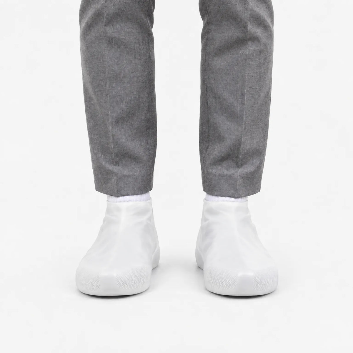 Front view of translucent white shoe covers worn with white socks and grey trousers, showing the patterned grip at the toe. 8