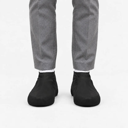 Front view of black shoe covers worn with white socks and grey trousers, with textured grip panels at the toes. 9