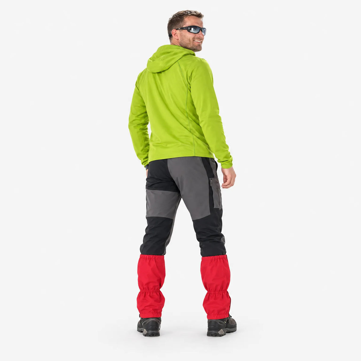 Rear view of a smiling man in sunglasses and a lime-green hoodie, wearing red gaiters over grey trousers and walking boots. 4
