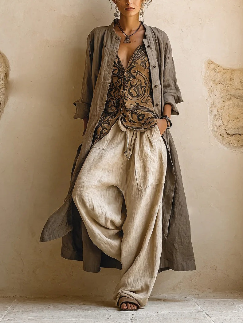 Model facing forward in a long taupe linen coat open over a patterned sleeveless top and wide beige trousers 1