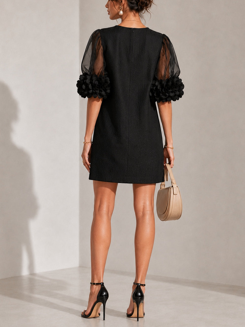 Back view of the black dress on a model, showing the plain back with centre seam and both floral-trimmed sheer sleeves. 3