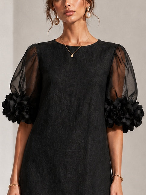 Close-up of the dress's round neckline, sheer puff sleeves and three-dimensional black floral appliqué cuffs on a model. 5