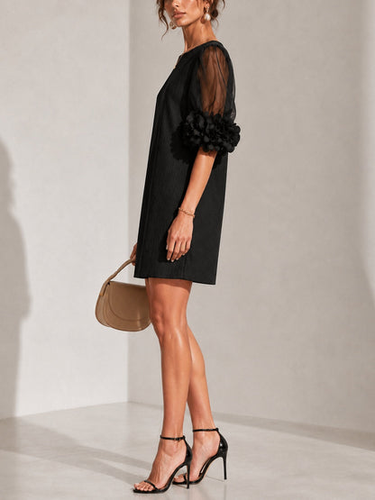 Side view of the black dress on a model in black heeled sandals, showing the sheer sleeve and ruffled floral cuff. 2