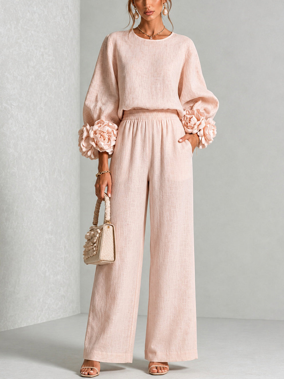 Model standing front-on in the blush pink set, hand in pocket, holding a woven handbag 1