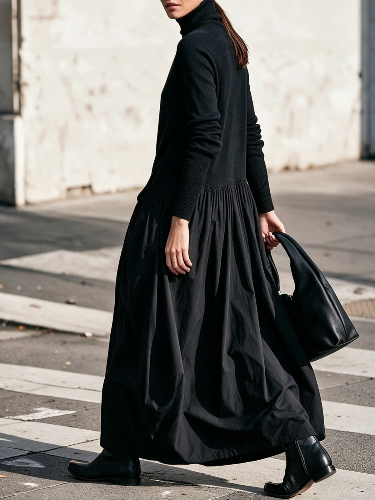 Black dress seen from the side on a walking model, showing the ribbed cuffs and gathered skirt 2