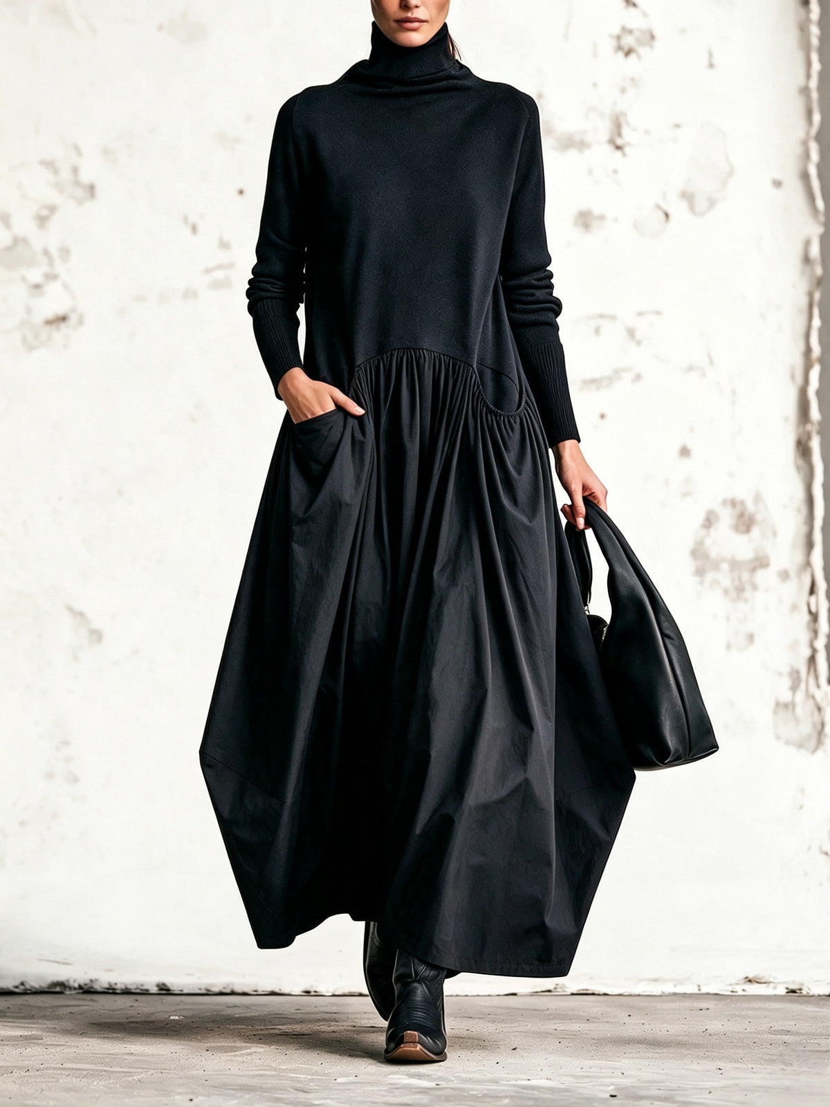 Model in the black dress facing forward, one hand in a gathered side pocket, holding a black bag 1