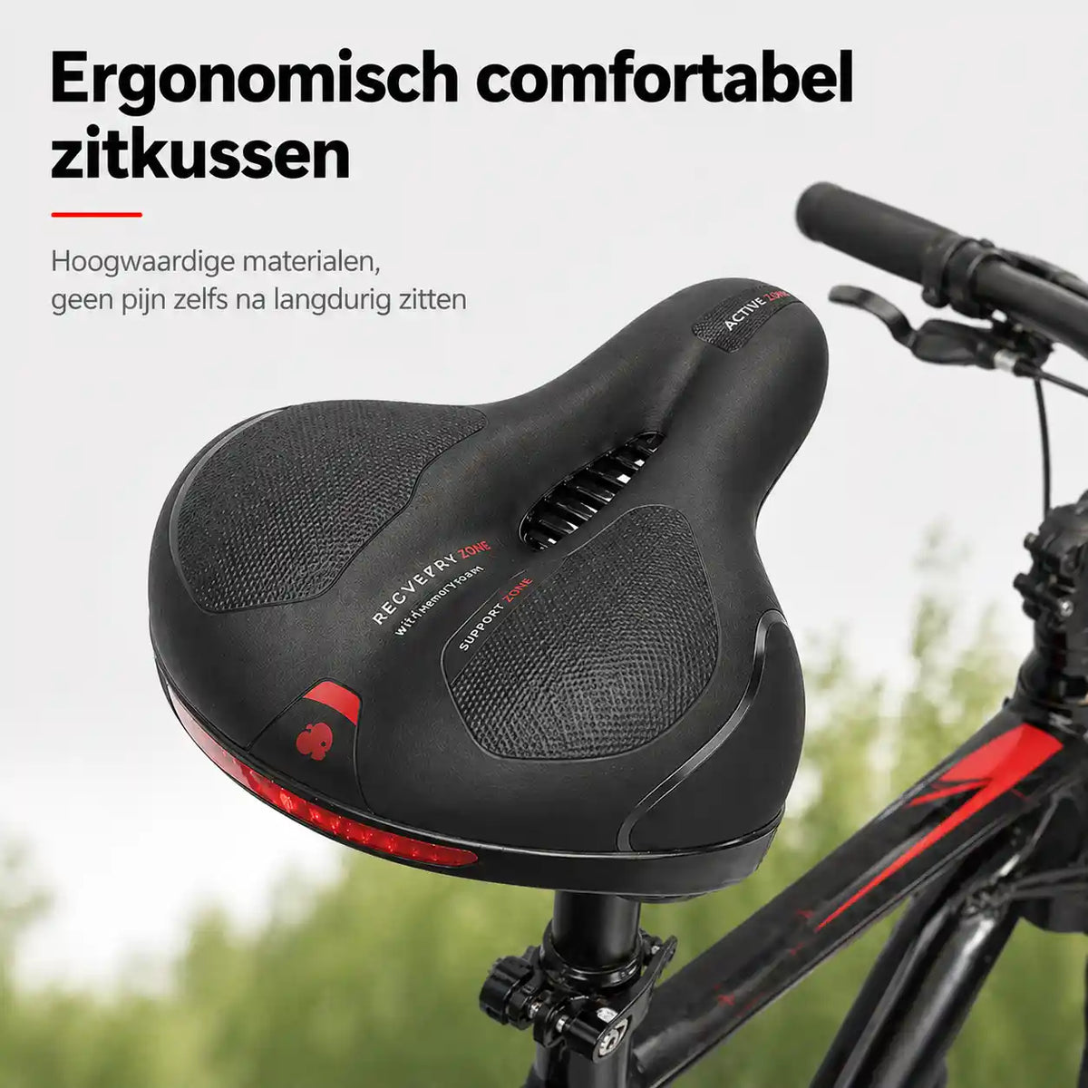 Black saddle with red trim, central ventilation cutout and textured support pads, fitted to a mountain bike against a green backdrop. 1