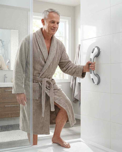 Man in a grey bathrobe steps out of a glass shower enclosure, holding the grab bar fitted upright on a white tiled wall. 15