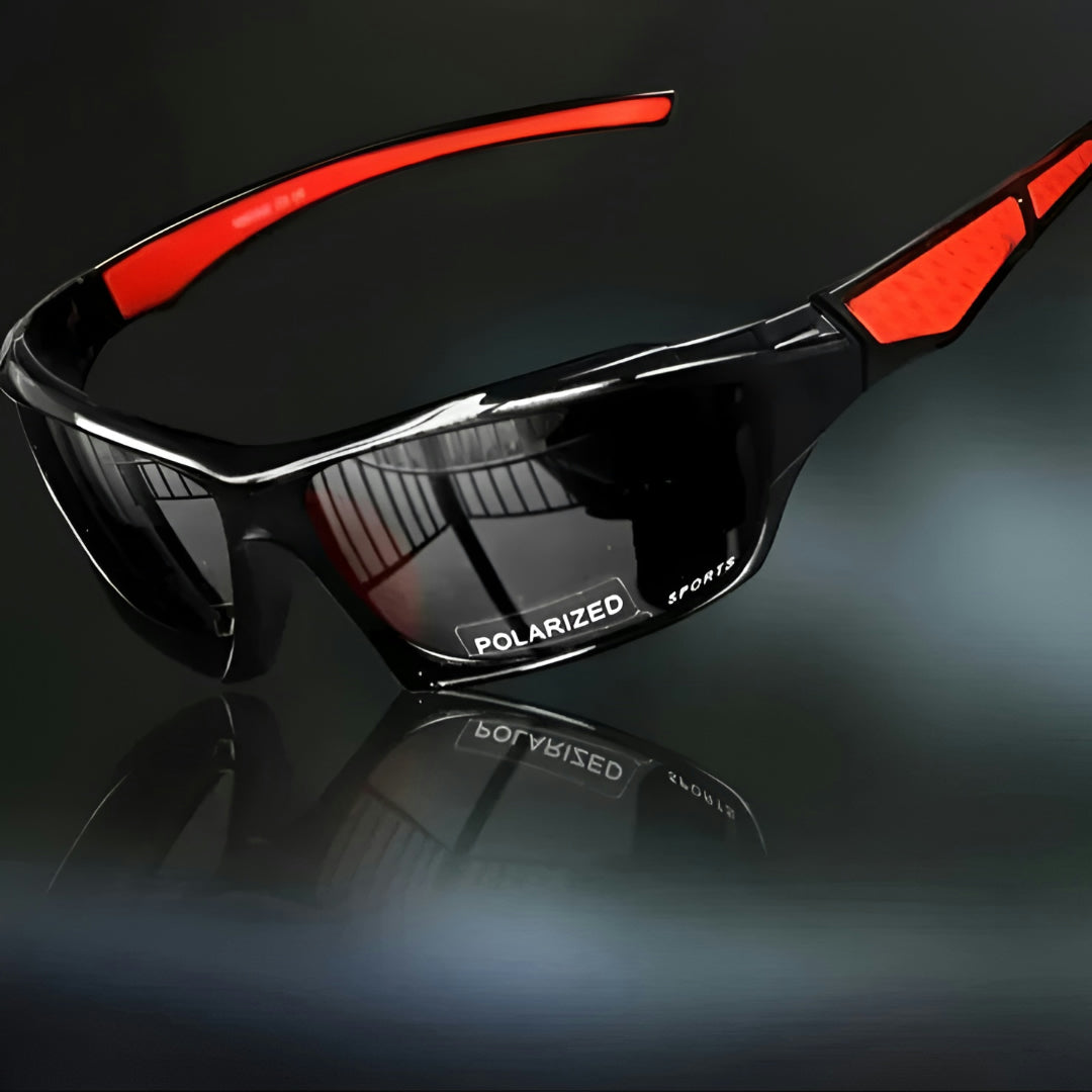 Black wraparound sports sunglasses with dark grey lenses and red arm inserts, angled on a reflective dark surface 1
