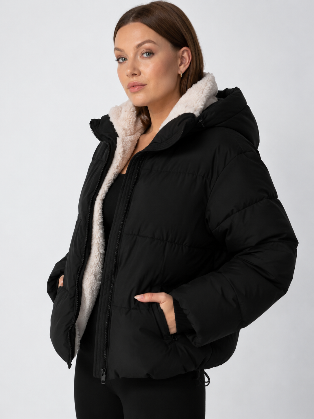 Angled view of the black puffer jacket with hood, cream fleece lining visible and a hand in the pocket 12