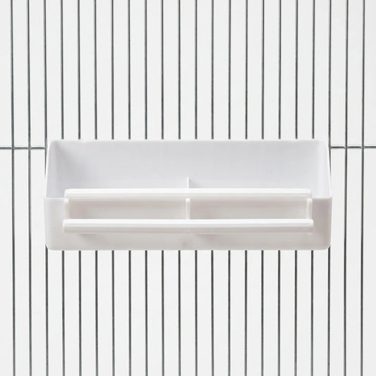 White plastic divided feeder with two perches, hooked onto the metal bars of a cage, seen straight from the front. 1