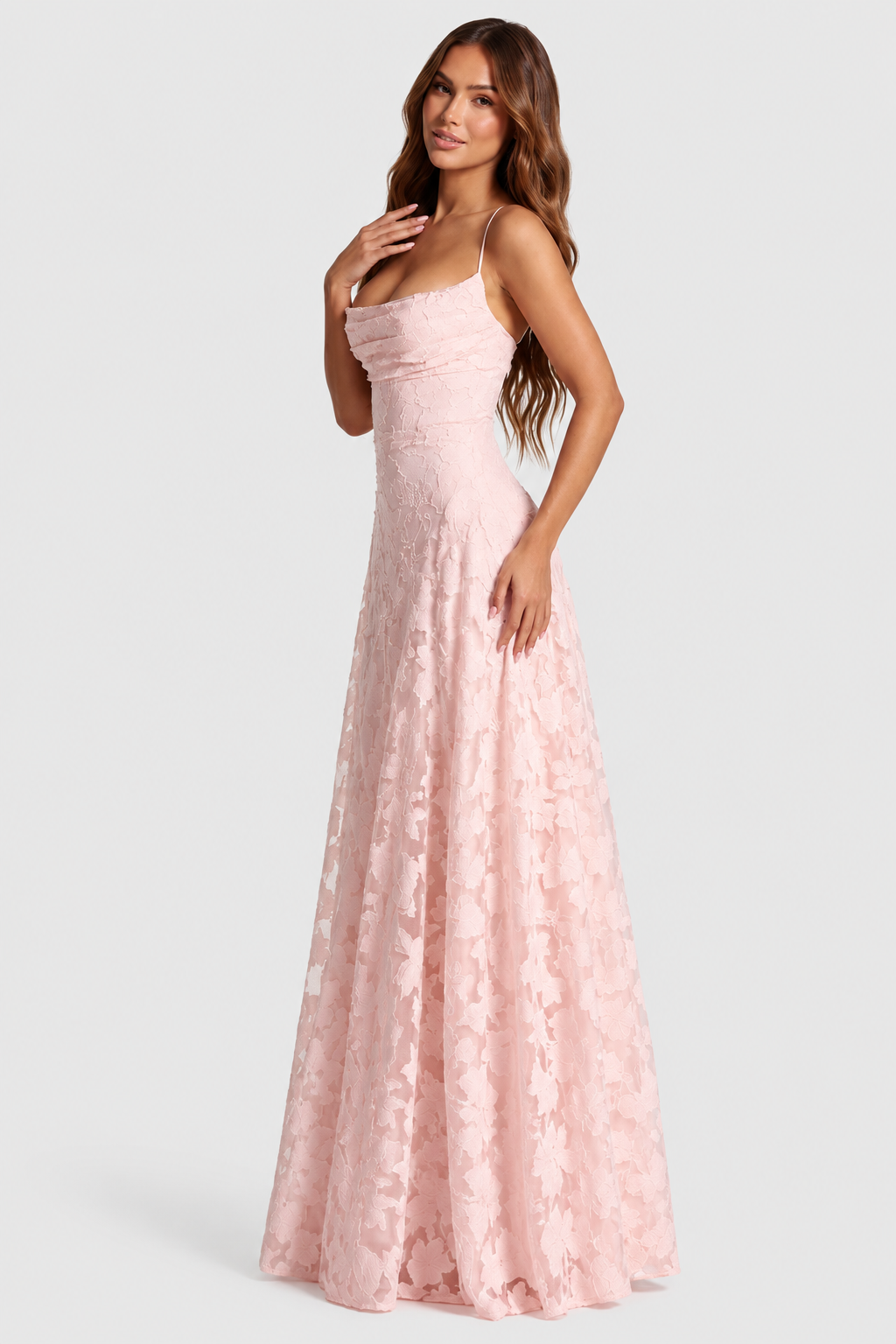 Model turned three-quarters in a pale pink floral lace gown with draped neckline and thin straps, hand resting at collarbone. 1