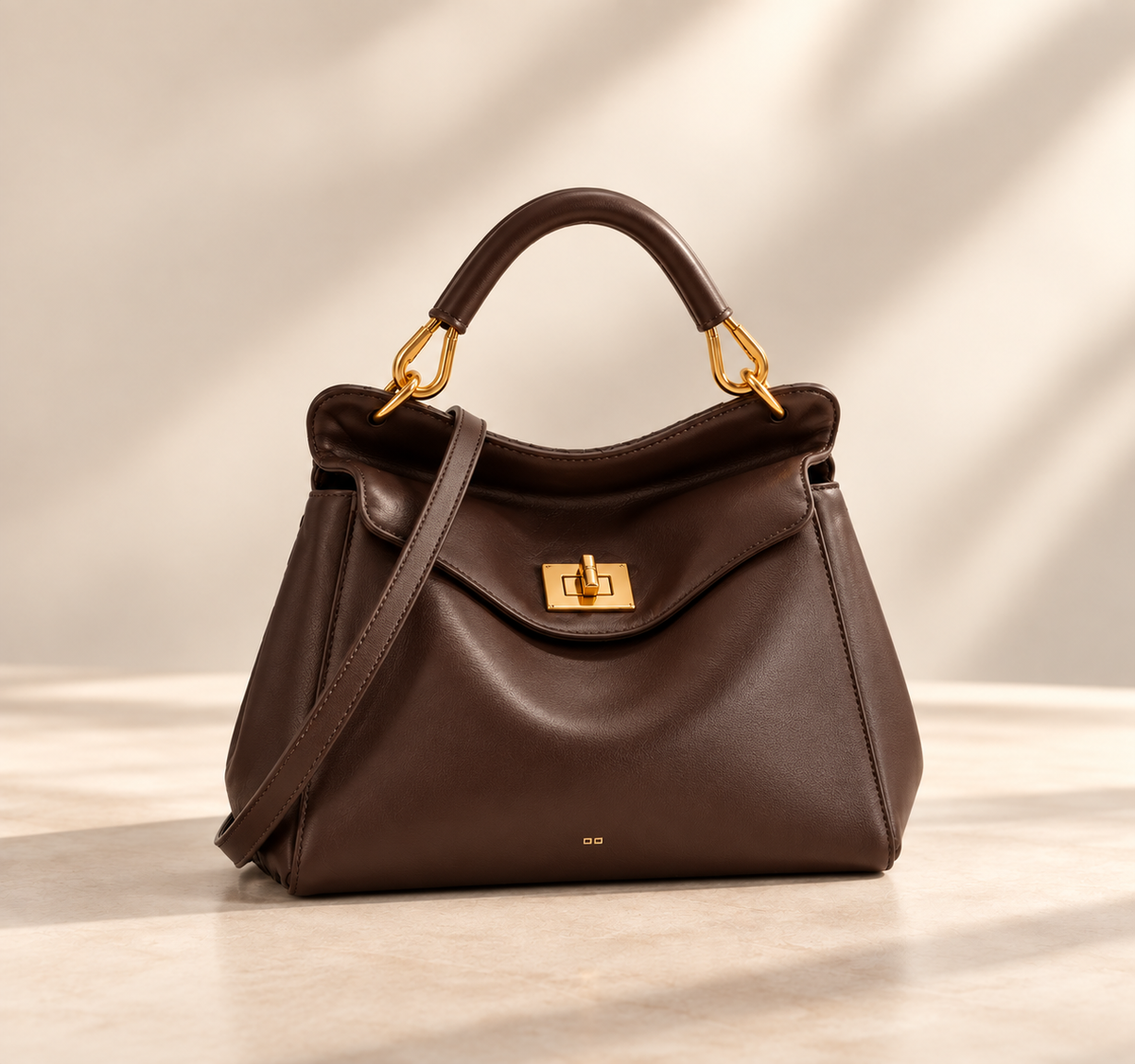 Smooth dark brown version with gold turn-lock and crossbody strap, shown on a pale studio surface 2