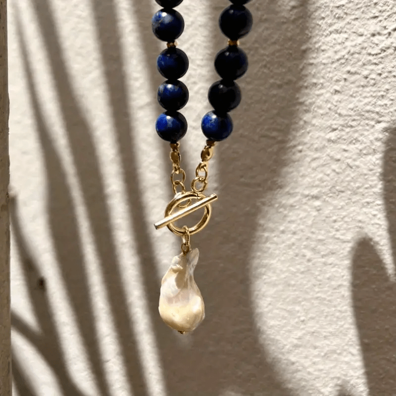 Necklace hanging against a textured wall with palm-leaf shadows, showing the toggle clasp and pearl 8
