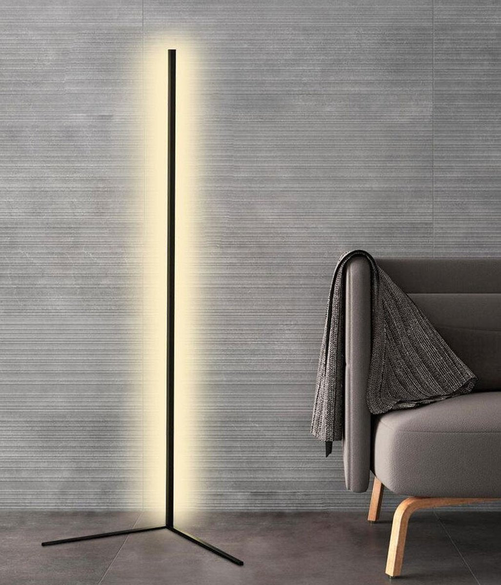 Tall black lamp with a warm white glow against a grey ribbed wall, next to an armchair 8