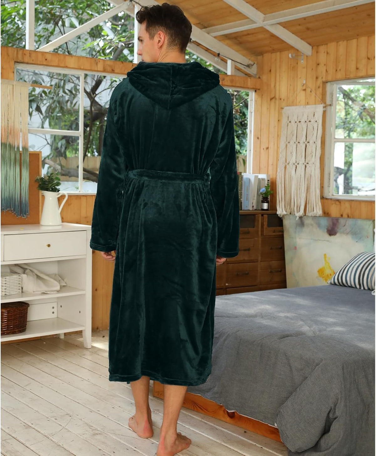 Back view of the dark green hooded robe on a model in a wood-panelled bedroom 2