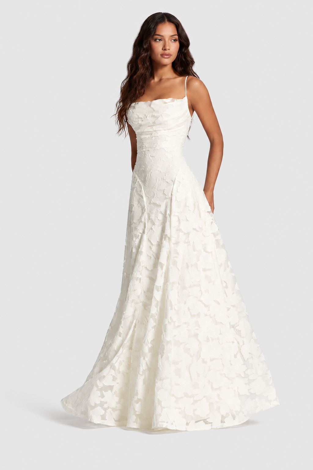 Model in a white raised floral lace gown with draped neckline, slim straps and a sweeping skirt, looking away. 19