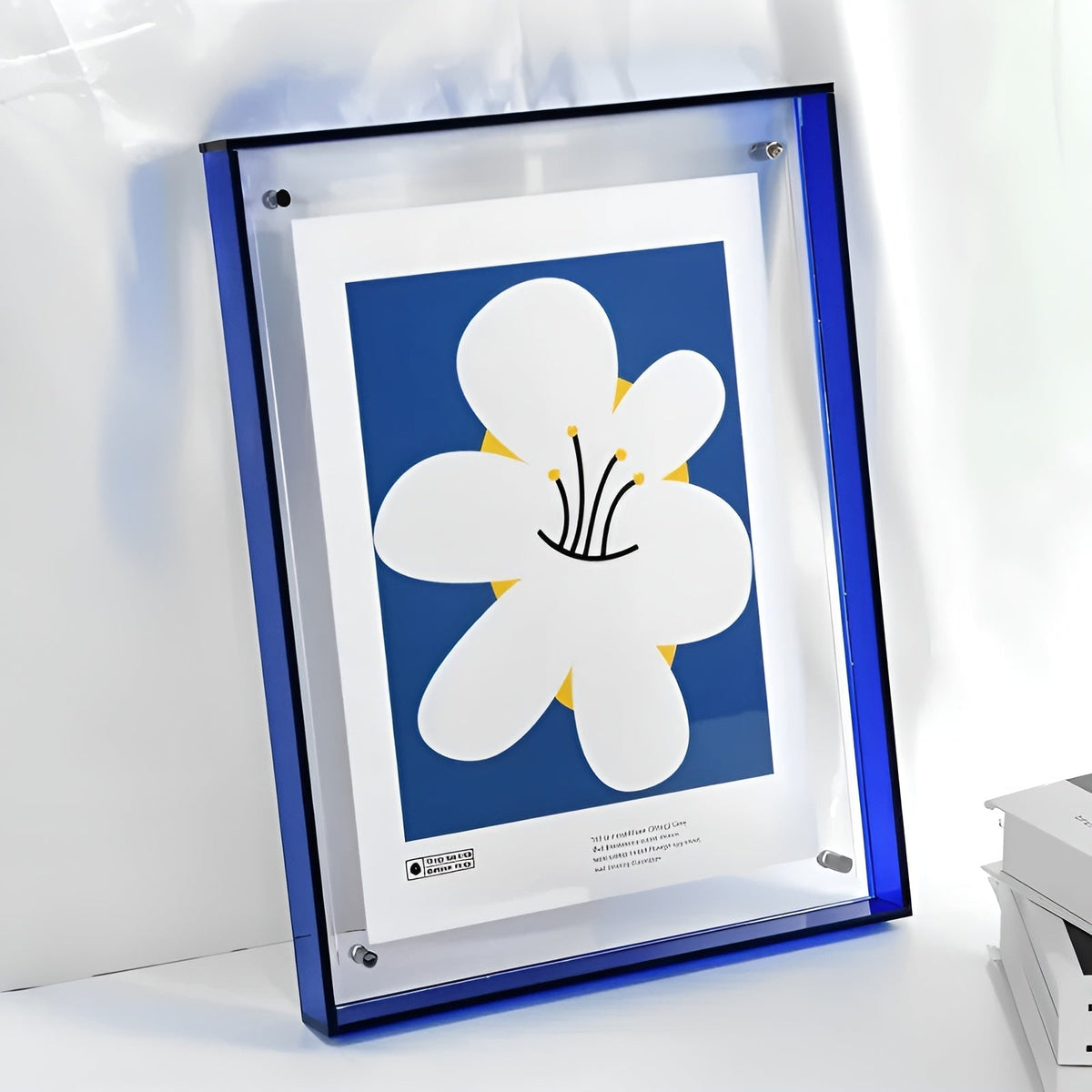 Royal blue acrylic frame leaning on a white surface, holding a print of a large white flower on a blue background. 14