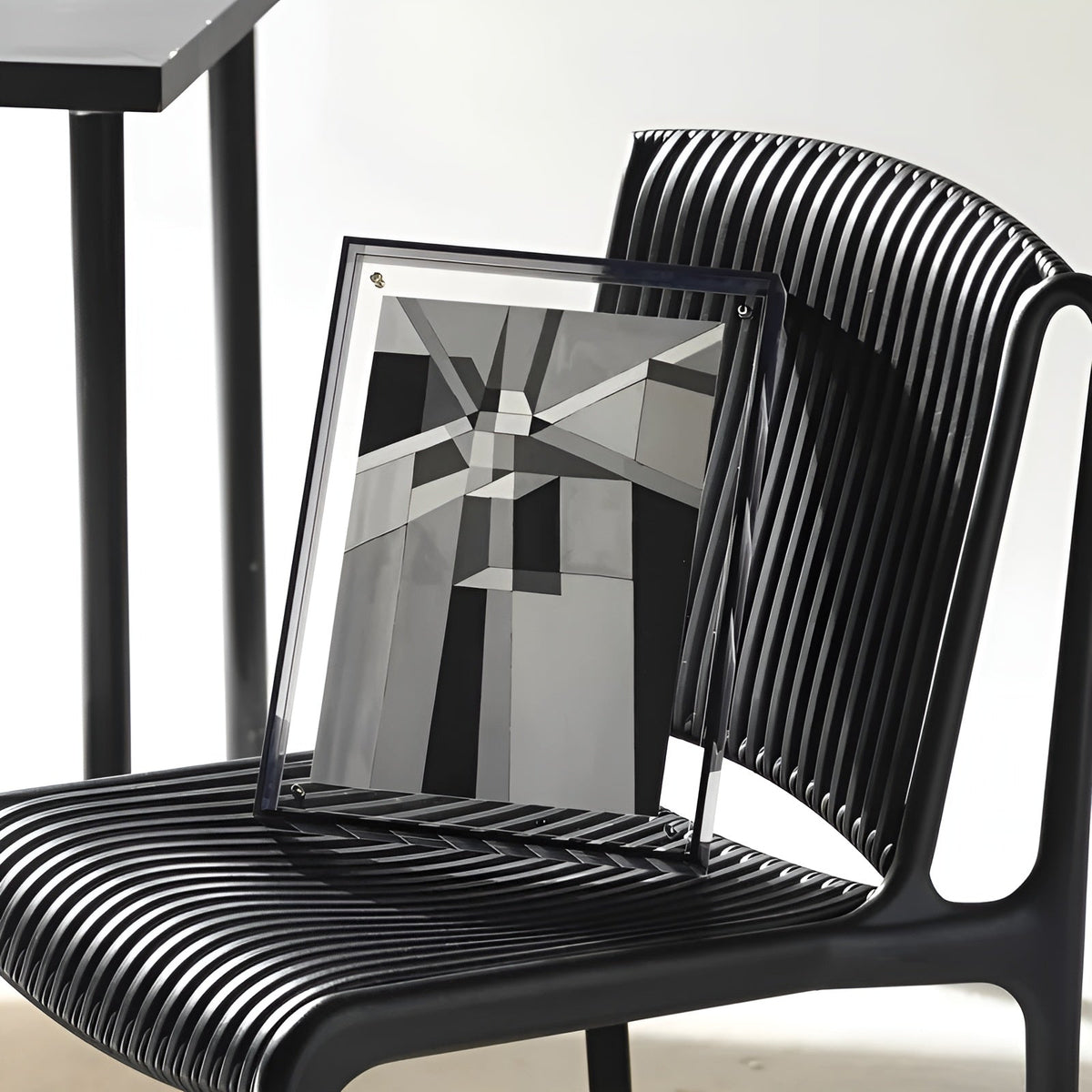 Dark-edged acrylic frame holding a black, white and grey geometric print, leaning on a black ribbed chair. 7