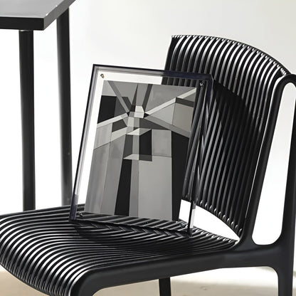Dark-edged acrylic frame holding a black, white and grey geometric print, leaning on a black ribbed chair. 7