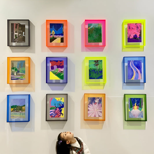 Wall of twelve acrylic frames in orange, pink, yellow, blue, green and grey, each holding a colourful painting, with a child looking up. 2