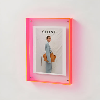 Neon pink acrylic frame mounted on a white wall, glowing softly and holding a fashion print of a woman carrying a tan bag. 18