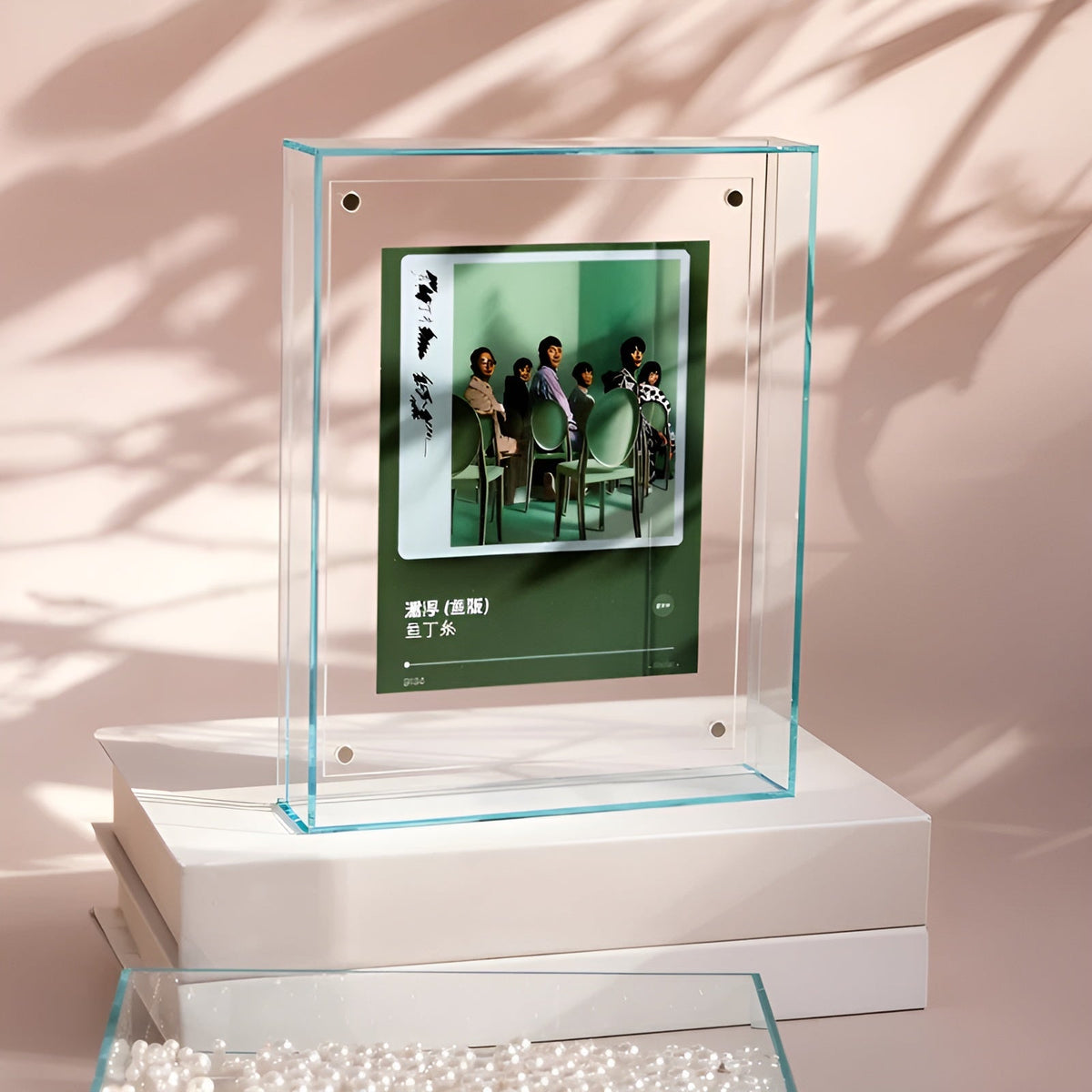 Freestanding clear acrylic block frame with a pale green edge, holding a green album-style print of seated people, against soft shadows. 13