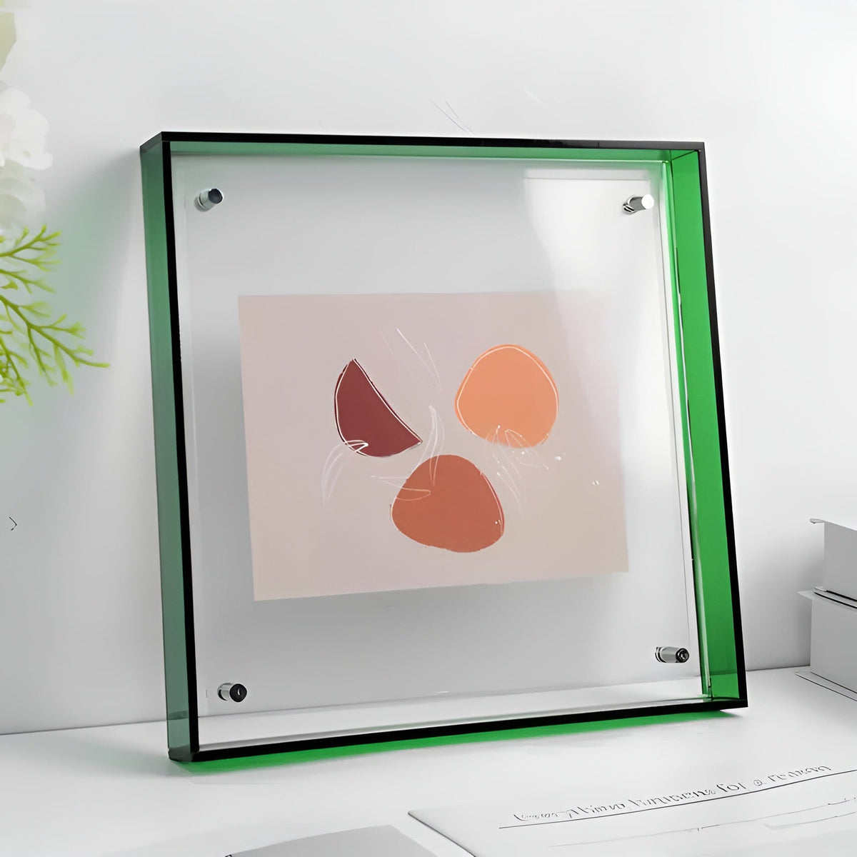 Square clear acrylic frame with a green edge and corner studs, holding a small abstract print and standing on a white shelf. 21