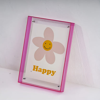 Pink-edged acrylic frame leaning against a white wall, holding a smiling flower print with studs at each corner. 19