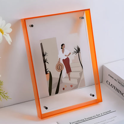Orange-edged acrylic frame on a white shelf, holding an illustrated print of a woman with a hat, beside white flowers. 10