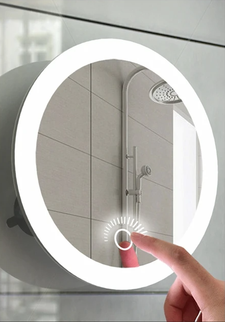 Illuminated round mirror stuck to a shower wall, with a finger pressing its touch control 1
