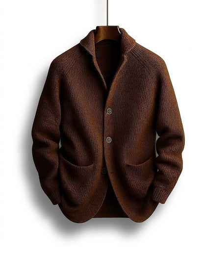 Brown ribbed cardigan with shawl collar, three buttons and two patch pockets, hanging on a wooden hanger, seen from the front. 1