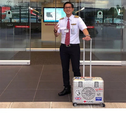 Smiling airline pilot in uniform standing beside a silver case covered in travel stickers, handle extended 4