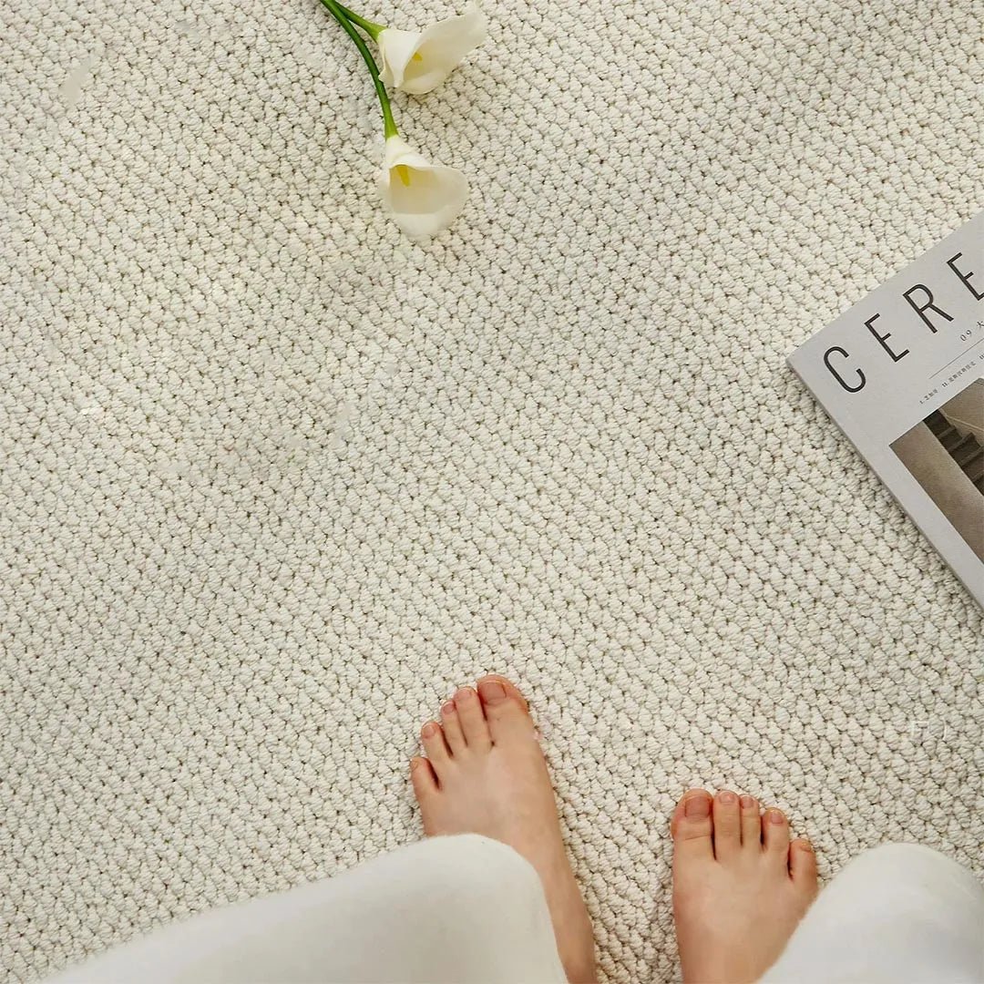 Close-up of a cream looped-pile surface with bare feet standing on it, beside white flowers 5