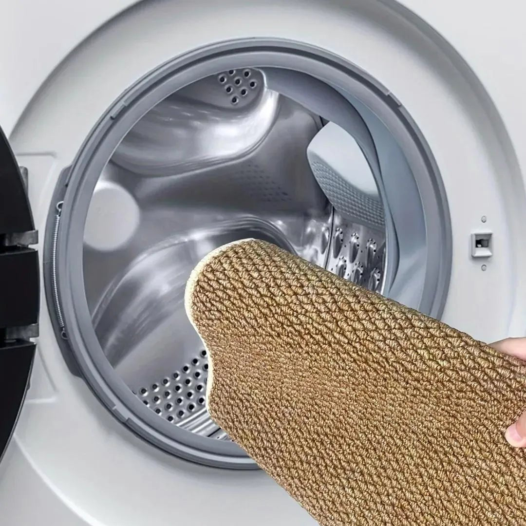 Hand holding a rolled tan mat towards the open drum of a washing machine 7