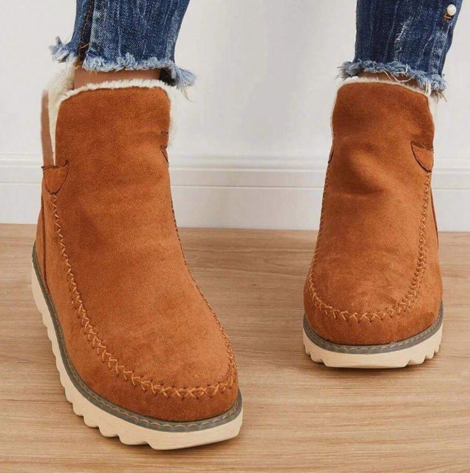 Front view of tan brown ankle boots on a model, showing the stitched moccasin-style toe and soft fleece lining at the top. 5